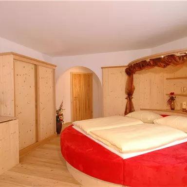 Ein gemütliches Schlafzimmer mit einem runden Bett und roten Akzenten. Die Möbel sind aus hellem Holz und schaffen eine warme Atmosphäre.