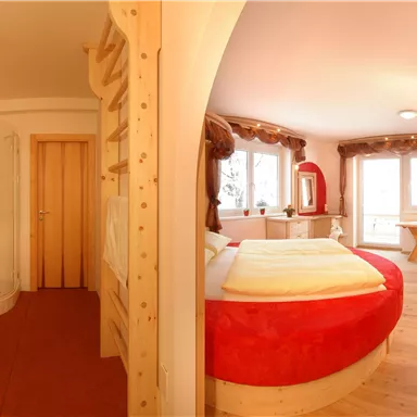 Ein gemütliches Zimmer mit einem großen Bett, einer Dusche und einem hellen Fenster. Die Einrichtung ist modern mit warmen Farben und Holzelementen.