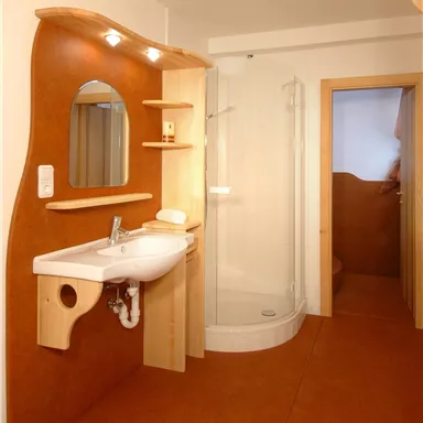 Ein modernes Badezimmer mit Waschbecken, Spiegel und Duschkabine. Die Wände sind in warmen Farben gehalten und der Boden ist orange.