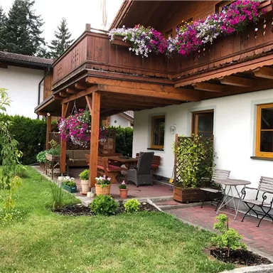 Ein gemütliches Haus mit einem schönen Balkon, der mit bunten Blumen geschmückt ist. Der Garten bietet eine einladende Sitzecke und eine grüne Rasenfläche.