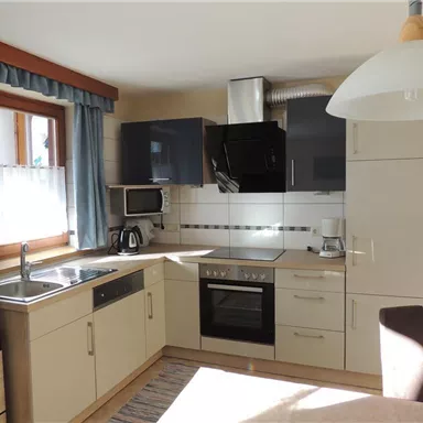 A modern kitchen with bright cabinets, a stove, and a sink. Windows with curtains provide natural light.