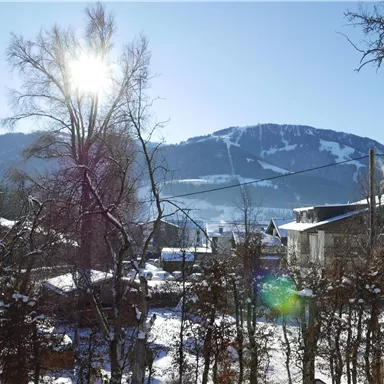 A snowy landscape with a sunny sky. In the background, there are mountains and some houses.