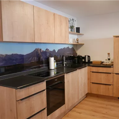 A modern kitchen with wooden cabinets and a dark countertop. In the background, a calming mountain motif can be seen.