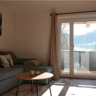 A cozy room with a gray sofa and a table. Large windows offer a view of the mountains and plenty of daylight.