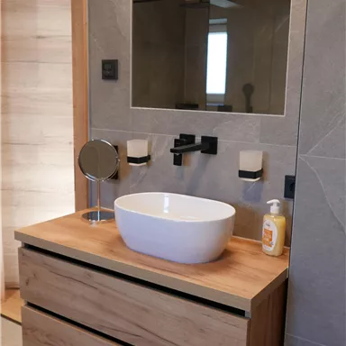 A modern bathroom with an elegant sink on a wooden piece of furniture. The large mirror and the gray walls create a stylish atmosphere.