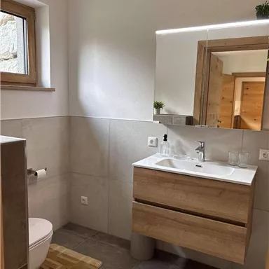Ein modernes Badezimmer mit einem Waschbecken und einem großen Spiegel. Es hat helle Wände und einen Holzlook, der eine angenehme Atmosphäre schafft.