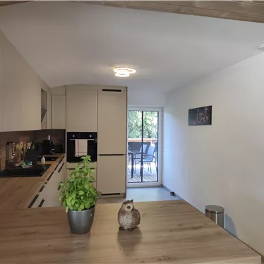 A modern kitchen with bright furniture and a large window front. On the table, there is a plant and a decoration.