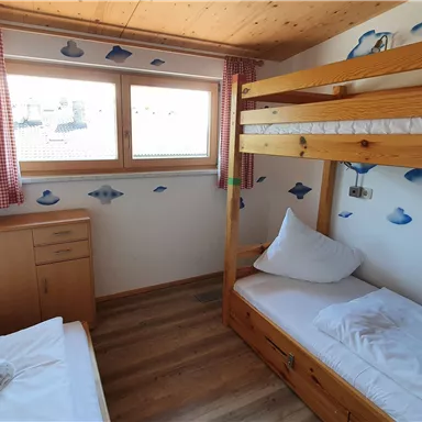 A cozy bedroom with a bunk bed and a single bed. The walls are decorated with cloud motifs and there are large windows for ample daylight.
