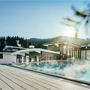 A modern outdoor pool surrounded by snow-capped mountains. The sun is shining, creating a relaxing atmosphere.