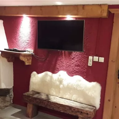 A cozy room with a fireplace and a TV on the wall. The walls are painted red, and a wooden bench adds to the warm atmosphere.