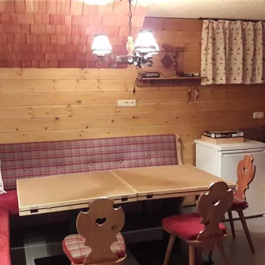 A cozy room with wood paneling and a sitting area. The table is in the middle and there is a small kitchen with a refrigerator.