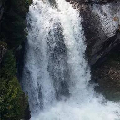 A rushing waterfall cascades over rocks into a clear water pool. Surrounded by green vegetation, the scene offers a peaceful natural backdrop.