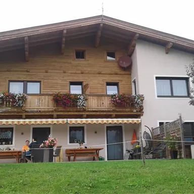 A large house with a wooden balcony and colorful flower boxes. The garden is green and inviting, with some seating options.