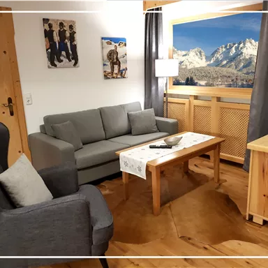 A cozy living room with a gray couch and a wooden coffee table. Through the window, you can see the mountains and the beautiful landscape.