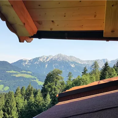A beautiful view of the mountains with a clear blue sky backdrop. In the foreground, a part of the roof and wood paneling is visible.