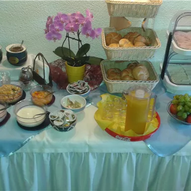 A rich breakfast buffet with various foods and drinks. There are rolls, fruits, jam, and yogurt on display, accompanied by a beautiful orchid.