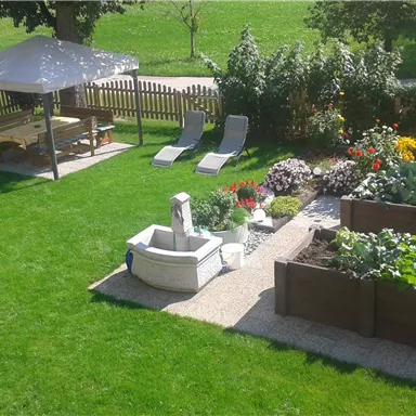 A well-maintained garden with a pavilion, loungers, and colorful flowers. Raised beds with vegetables and plants are also visible.