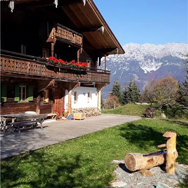 Ein traditionelles Chalet mit blühenden Balkonpflanzen und Blick auf die Berge. Der Himmel ist klar und blau, ideal für einen entspannten Tag in der Natur.