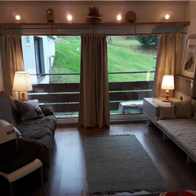 Ein gemütliches Wohnzimmer mit zwei Sitzbereichen und einem Blick auf eine grüne Wiese. Große Fenster lassen viel Licht herein und schaffen eine einladende Atmosphäre.