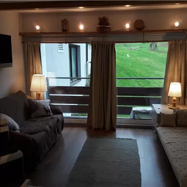 Ein gemütlicher Wohnraum mit zwei Sofas, beleuchtet von sanften Lampen. Große Fenster bieten einen Blick auf eine grüne Landschaft.