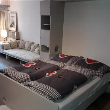 Ein modernes Schlafzimmer mit einem Doppelbett und liebevollem Bettzeug. Neben dem Bett steht eine gemütliche Couch und ein Tisch mit einer Lampe.