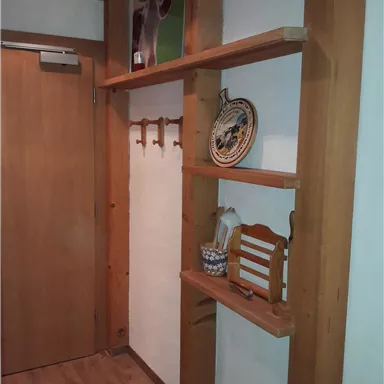 Ein gemütlicher Flur mit einem Holzregal, einer Tür und dekorativen Elementen. An der Wand hängen Mäntel und eine dekorierte Platte.