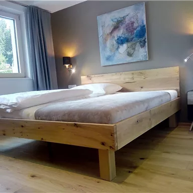 A cozy bedroom with a wooden bed and modern wall lamps. The green nature is visible through the window.