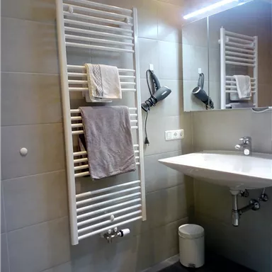 A modern bathroom with a towel warmer and a sink. The white towels are reflected on the wall, and the bathroom floor is tiled in gray.