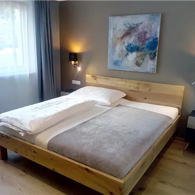 A modern bedroom with a wooden bed and a painting on the wall. The rooms are bright and friendly with natural light and stylish decor.