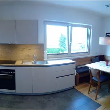 A modern kitchen with elegant white cabinets and a bright dining area. Large windows provide plenty of natural light.