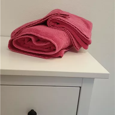 A stack of pink towels lies on a white dresser. The towels are neatly rolled up and appear fresh and clean.