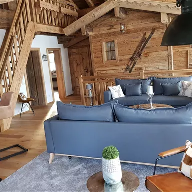Ein gemütlicher Wohnraum mit Holzverkleidung und modernen Möbeln. Im Hintergrund sind eine Treppe und verschiedene Sitzgelegenheiten zu sehen.