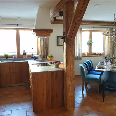 Eine moderne Küche mit Holzvertäfelungen und einem Essbereich. Große Fenster sorgen für viel Tageslicht und eine gemütliche Atmosphäre.