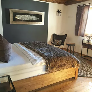 Ein gemütliches Schlafzimmer mit einem modernen Bett und weichen Bettwaren. Die Wände sind in dunklen Tönen gehalten, und es gibt eine stylische Sitzgelegenheit und einen kleinen Tisch.