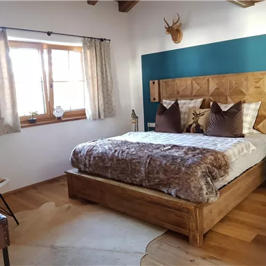 Ein gemütliches Schlafzimmer mit einem großen Bett und Holzdekor. Die Wände sind in sanften Farben gestrichen, und ein Fenster lässt viel Tageslicht herein.