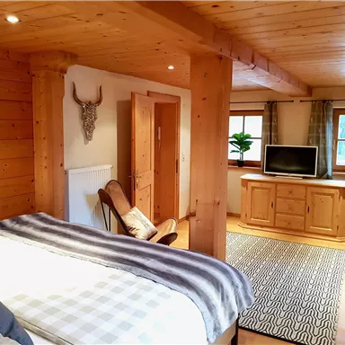 Ein gemütliches Schlafzimmer aus Holz mit einem großen Bett und einem Fernseher. Die Einrichtung ist rustikal und einladend, ideal zum Entspannen.