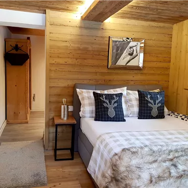 Ein gemütliches Schlafzimmer mit Holzwänden und einem großen Bett. Es gibt dekorative Kissen und einen kleinen Tisch neben dem Bett.