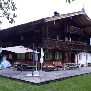 Ein traditionelles Holzhaus in einer malerischen Landschaft. Der große Garten ist mit Holzliegen und einem Sonnenschirm ausgestattet.