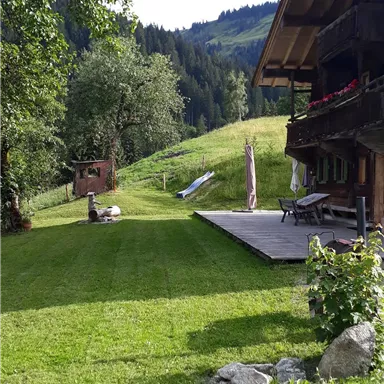 Ein schöner Garten mit gepflegtem Rasen und Blick auf die Berge. Im Hintergrund steht ein traditionelles Holzhaus.