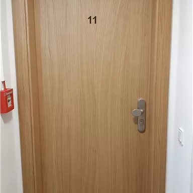 Eine schlichte Holzhaustür mit der Nummer 11. Die Tür ist hell und hat einen modernen Türgriff.