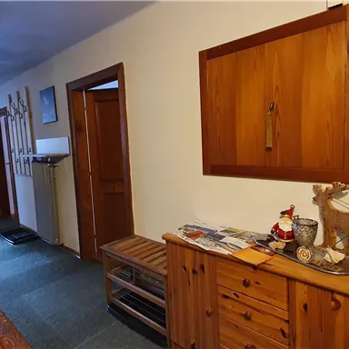 A cozy hallway with wooden paneling and a wooden dresser. Skis hang on the wall, and various decorations are on the table.