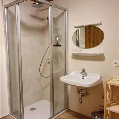 A modern bathroom with a glass shower and a sink. The walls are light and the floor is made of wood.