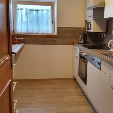 A modern kitchen with bright furniture and wooden details. The window provides plenty of daylight.