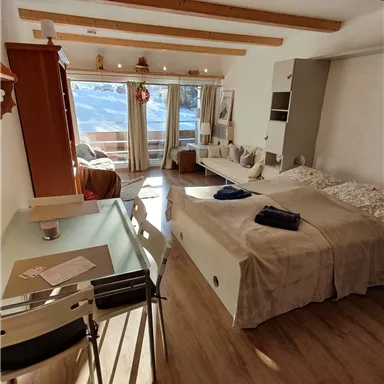 Eine helle und gemütliche Wohnung mit Holzdeckenbalken. Der Raum enthält ein Bett, einen Esstisch und große Fenster mit Aussicht.