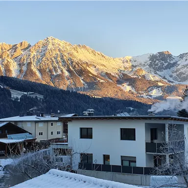Eine malerische Winterlandschaft mit schneebedeckten Bergen im Hintergrund. Im Vordergrund steht ein modernes Wohnhaus.