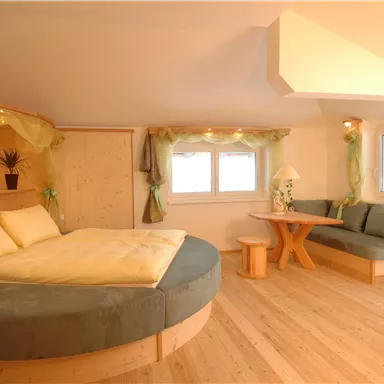Ein gemütliches Zimmer mit einem runden Bett und einer Sitzgelegenheit. Warmes Licht und natürliche Materialien schaffen eine einladende Atmosphäre.