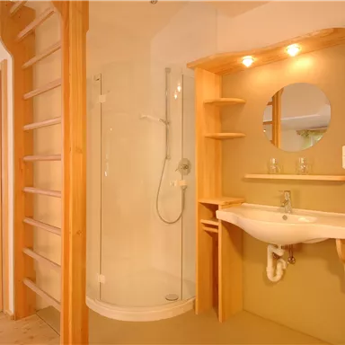 Ein modernes Badezimmer mit einer Duschkabine und einem Waschbecken. Die Wände sind in sanften Farben gehalten und es gibt Holz-Elemente.