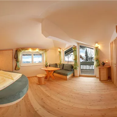 Ein komfortables Zimmer mit einem Doppelbett und einem gemütlichen Sitzbereich. Große Fenster sorgen für viel Tageslicht und einen Blick nach draußen.
