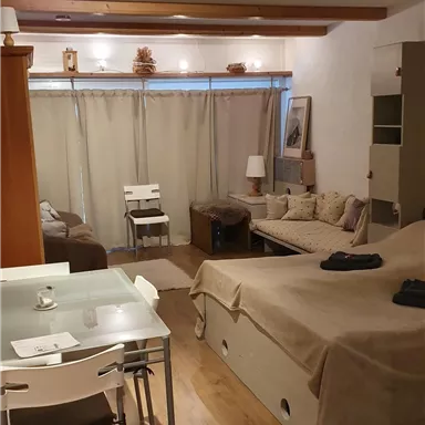 Ein gemütliches Apartment mit Holzdecke und warmem Licht. Der Raum enthält einen Wohnbereich mit einem Sofa, Tisch und Stühlen.