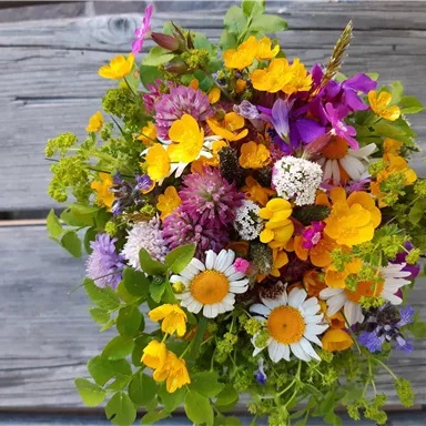 Ein bunter Strauß mit verschiedenen Wildblumen in leuchtenden Farben. Die Blumen sind üppig und frisch auf einem rustikalen Holztisch arrangiert.